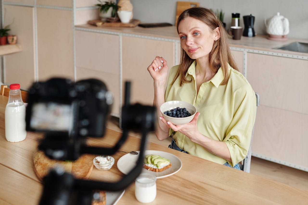 Woman vlogging a healthy breakfast setup with blueberries and milk in a cozy kitchen.