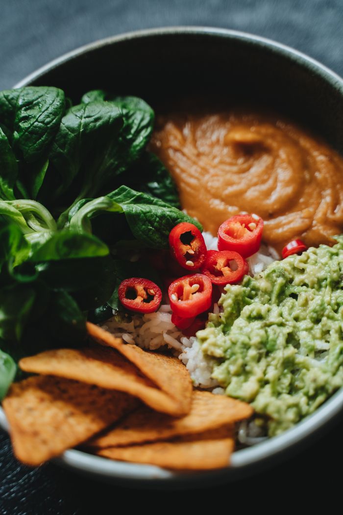 Services A vibrant vegan Buddha bowl featuring fresh spinach, guacamole, and chili peppers.
